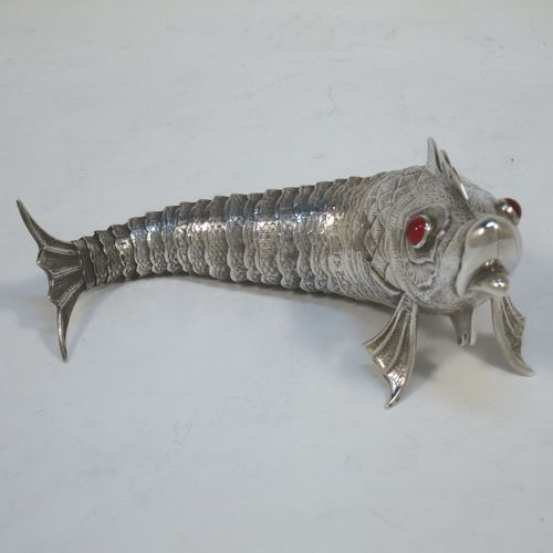 A very pretty Antique Edwardian Silver Articulated fish, having hand-chased scales and fins, and with two red glass eyes (possibly garnets). Made in Spain in ca. 1900. On one of the lower fins you can see the hallmark of a Pentagram that is a Spanish quality mark indicating a minimum of 915 Silver purity (Sterling Standard is 925). The dimensions of this fine hand-made antique Articulated Silver fish are length 17 cms (6.75 inches), height 5.5 cms (2.25 inches), and it weighs approx. 92g (3 troy ounces).   