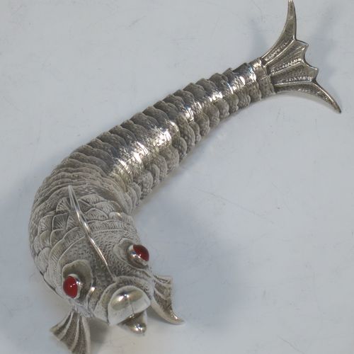 A very pretty Antique Edwardian Silver Articulated fish, having hand-chased scales and fins, and with two red glass eyes (possibly garnets). Made in Spain in ca. 1900. On one of the lower fins you can see the hallmark of a Pentagram that is a Spanish quality mark indicating a minimum of 915 Silver purity (Sterling Standard is 925). The dimensions of this fine hand-made antique Articulated Silver fish are length 17 cms (6.75 inches), height 5.5 cms (2.25 inches), and it weighs approx. 92g (3 troy ounces).   