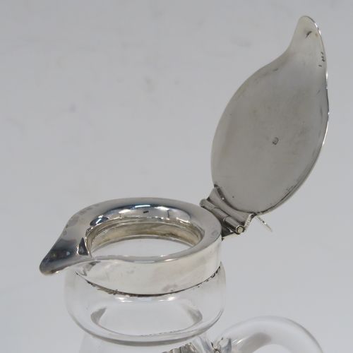 A handsome Antique Sterling Silver whisky toddy or noggin, having a round based hand-cut crystal body with tapering sides and loop handle, mounted with a silver collar and hinged flat lid with thumb-piece, all sitting on a flat star-cut base, and together with its original silver whisky label on a chain. This elegant silver and crystal whisky toddy was made by M and S Ltd. of Birmingham in 1913. The dimensions of this fine hand-made silver and crystal whisky noggin or toddy is height 11.5 cms (4.5 inches), and diameter at bases 7 cms (2.75 inches).