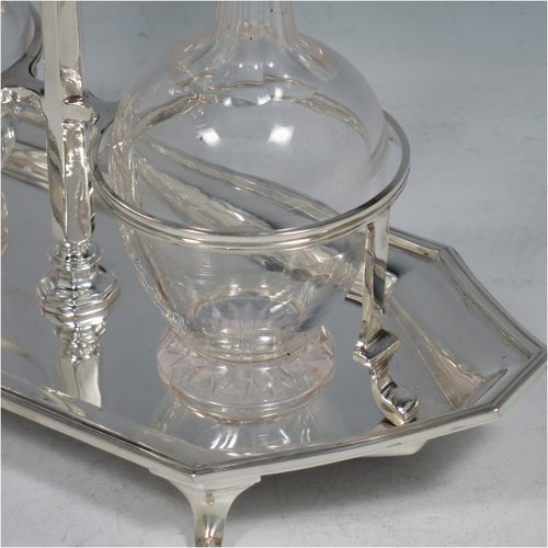 A Sterling Silver oil and vinegar set, having an octagonal boat-shaped body with applied reed-edged borders, a two-bottle frame with loop handle, a pair of hand-cut round crystal bottles with stoppers, and all sitting on four cast scroll feet. Made by Goldsmiths & Silversmiths of London in 1929. The dimensions of this fine hand-made silver oil and vinegar set are length 23 cms (9 inches), height 20 cms (8 inches), width 10 cms (4 inches), and the base weighs approx. 495g (16 troy ounces).