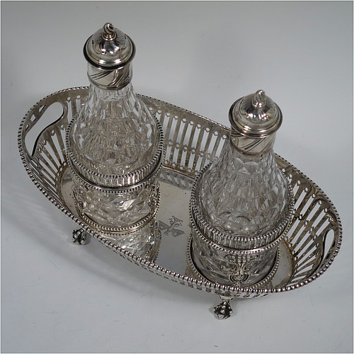 An Antique Georgian Sterling Silver oil and vinegar set, having an oval boat-shaped body with hand-pierced decoration and applied bead-edged borders, with cut-out loop side handles, a pair of hand-cut crystal bottles with stoppers in matching round galleried frames, and all sitting on four cast claw and ball feet. Made by Thomas Northcote of London in 1792. The dimensions of this fine hand-made antique silver oil and vinegar set are length 21.5 cms (8.5 inches), height (excl. bottles) 9 cms (3.5 inches), width 11.5 cms (4.5 inches), and with a total weight of approx. 400g (12.9 troy ounces). Please note that this item is crested.