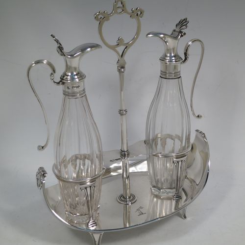 A very handosme Antique Sterling Silver oil and vinegar set in a neoclassical style, having an oval boat-shaped body with applied reed-edged borders, a two-bottle frame with hand-pierced handle, a pair of hand-cut round crystal bottles with panelled bodies and original hinged lid mounts with scroll handles, and all sitting on four flange feet. Made by Goldsmiths & Silversmiths of Sheffield in 1919. The dimensions of this fine hand-made antique silver oil and vinegar set are length 20 cms (8 inches), height 25.5 cms (10 inches), width 14 cms (5.5 inches), and it weighs approx. 250g (8 troy ounces).    