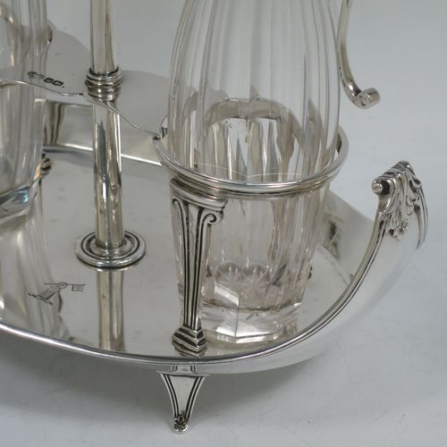 A very handosme Antique Sterling Silver oil and vinegar set in a neoclassical style, having an oval boat-shaped body with applied reed-edged borders, a two-bottle frame with hand-pierced handle, a pair of hand-cut round crystal bottles with panelled bodies and original hinged lid mounts with scroll handles, and all sitting on four flange feet. Made by Goldsmiths & Silversmiths of Sheffield in 1919. The dimensions of this fine hand-made antique silver oil and vinegar set are length 20 cms (8 inches), height 25.5 cms (10 inches), width 14 cms (5.5 inches), and it weighs approx. 250g (8 troy ounces).    