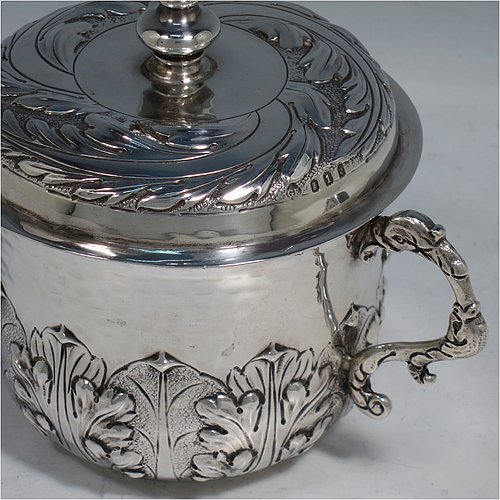 An Antique Edwardian Britannia Standard Silver porringer, having a round baluster body with a hand-hammered finish and hand-chased anthemion and floral decoration, a lift-off lid with matching floral work and a cast round finial, and two cast floral handles. Made by George Fox of London in 1906. The dimensions of this fine hand-made antique Britannia silver porringer and lid are height 11.5 cms (4.5 inches), spread across arms 16 cms (6.3 inches), and it weighs approx. 370g (12 troy ounces).