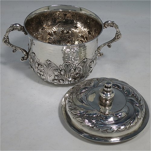 An Antique Edwardian Britannia Standard Silver porringer, having a round baluster body with a hand-hammered finish and hand-chased anthemion and floral decoration, a lift-off lid with matching floral work and a cast round finial, and two cast floral handles. Made by George Fox of London in 1906. The dimensions of this fine hand-made antique Britannia silver porringer and lid are height 11.5 cms (4.5 inches), spread across arms 16 cms (6.3 inches), and it weighs approx. 370g (12 troy ounces).