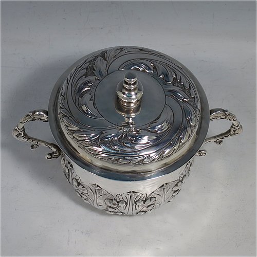 An Antique Edwardian Britannia Standard Silver porringer, having a round baluster body with a hand-hammered finish and hand-chased anthemion and floral decoration, a lift-off lid with matching floral work and a cast round finial, and two cast floral handles. Made by George Fox of London in 1906. The dimensions of this fine hand-made antique Britannia silver porringer and lid are height 11.5 cms (4.5 inches), spread across arms 16 cms (6.3 inches), and it weighs approx. 370g (12 troy ounces).