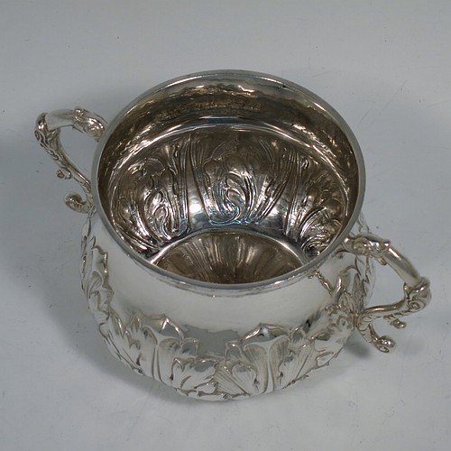 A heavy Sterling Silver porringer, having a round bellied body with a slight hand-hammered finish and hand-chased anthemion and floral decoration, and two cast side-handles with stylised dolphin heads. Made by Robert Comyns of London in 1931. The dimensions of this fine hand-made silver porringer are height 7 cms (2.75 inches), spread across arms 14 cms (5.5 inches), and it weighs approx. 247g (8 troy ounces).