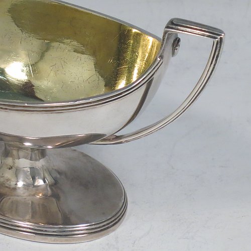 An Antique Georgian Sterling Silver pair of salt cellars, in a boat-shaped style, having plain oval bodies, with gold-gilt interiors, applied reeded borders, and reeded side-handles, all sitting on pedestal feet. Made by either Henry Nutting OR Hannah Northcote of London in 1803. The dimensions of these fine hand-made antique silver salt cellars are length 14 cms (5.5 inches), width 6 cms (2.3 inches), height 7.5 cms (3 inches), and they weigh a total of approx. 217g (7 troy ounces).