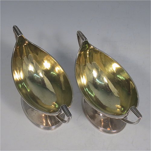 An Antique Georgian Sterling Silver pair of salt cellars, in a boat-shaped style, having plain oval bodies, with gold-gilt interiors, applied reeded borders, and reeded side-handles, all sitting on pedestal feet. Made by either Henry Nutting OR Hannah Northcote of London in 1803. The dimensions of these fine hand-made antique silver salt cellars are length 14 cms (5.5 inches), width 6 cms (2.3 inches), height 7.5 cms (3 inches), and they weigh a total of approx. 217g (7 troy ounces).