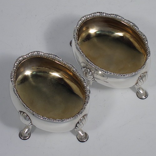 An Antique Georgian Sterling Silver pair of salt cellars, having plain oval bodies, with gold-gilt interiors, applied shaped gadroon borders, and all sitting on four cast hoof feet with shell shoulders. Made by Robert and David Hennell of London in 1767. The dimensions of these fine hand-made antique silver salt cellars are length 9 cms (3.5 inches), width 8 cms (3 inches), height 4.5 cms (1.75 inches), and they weigh a total of approx. 177g (5.7 troy ounces).