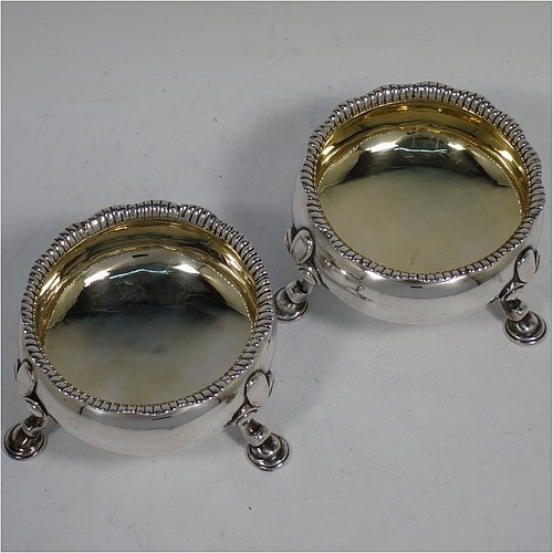 A large and handsome pair of Antique Georgian Sterling Silver salt cellars, having plain round bodies, with gold-gilt interiors, applied shaped gadroon borders, and all sitting on three cast hoof feet with foliate shoulders. Made by Peter Taylor of London in 1750. The dimensions of these fine hand-made antique silver salt cellars are diameter 8 cms (3 inches), height 5 cms (2 inches), and they weigh a total of approx. 224g (7.2 troy ounces). Please note that these items are crested.