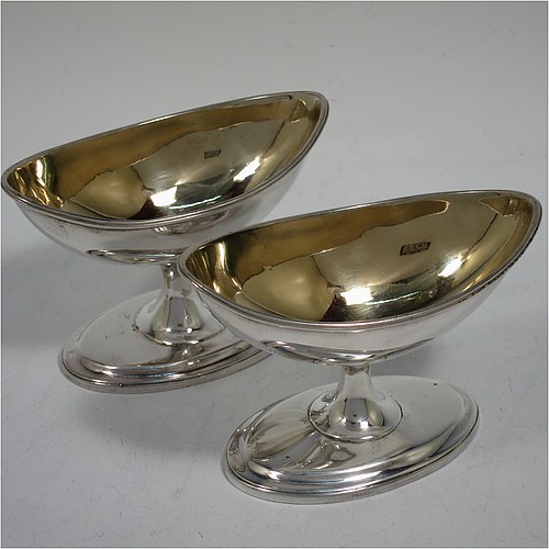 A rare and very handsome Antique Georgian Sterling Silver pair of Irish salt cellars, in a boat-shaped neoclassical style, having plain oval bodies, with gold-gilt interiors and blue-glass liners, with applied reeded borders, all sitting on pedestal feet. Made by John Stoyte of Dublin in 1798. The dimensions of these fine hand-made antique silver Irish salt cellars are length 10 cms (4 inches), width 5.5 cms (2.25 inches), height 6.5 cms (2.5 inches), and they weigh a total of approx. 142g (4.6 troy ounces).