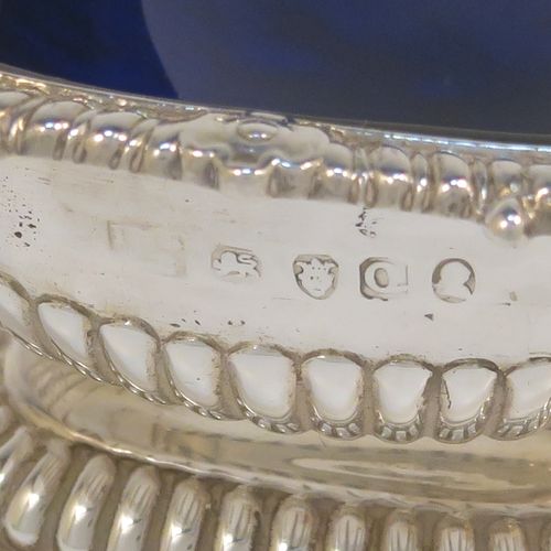 A large and handsome pair of Antique Georgian Sterling Silver salt cellars in a Regency style, having rectangular bodies, with blue-glass liners, applied shell and gadroon borders, half-fluted hand-chased decoration, and all sitting on pedestal bases. These elegant antique silver salt cellars were made in London in 1811. The dimensions of these fine hand-made antique silver salt cellars are length 9.5 cms (3.75 inches), width 7 cms (2.75 inches), height 5 cms (2 inches), and they weigh a total of approx. 237g (7.6 troy ounces). Please note that these items are part crested.