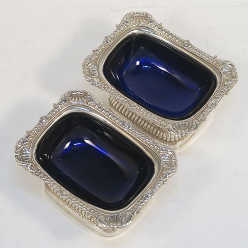 A large and handsome pair of Antique Georgian Sterling Silver salt cellars in a Regency style, having rectangular bodies, with blue-glass liners, applied shell and gadroon borders, half-fluted hand-chased decoration, and all sitting on pedestal bases. These elegant antique silver salt cellars were made in London in 1811. The dimensions of these fine hand-made antique silver salt cellars are length 9.5 cms (3.75 inches), width 7 cms (2.75 inches), height 5 cms (2 inches), and they weigh a total of approx. 237g (7.6 troy ounces). Please note that these items are part crested.