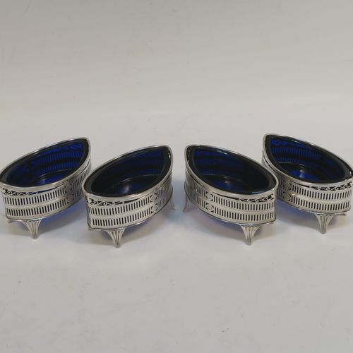 An elegant set of four Antique Edwardian Sterling Silver salt cellars in a Neoclassical style, having oval boat-shaped bodies with hand-pierced galleried sides, internal blue glass liners, and sitting on four fluted flange feet. These beautiful antique silver salt cellars were made by Jackson and Fullerton of London in 1909. The dimensions of this fine hand-made set of four silver salt cellars are length 9 cms (3.5 inches), height 5 cms (2 inches), width 5 cms (2 inches), and they weigh a total of approx. 214g (6.9 troy ounces).   