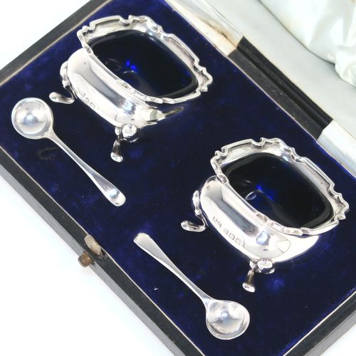 A very pretty pair of Antique Sterling Silver salt cellars, having plain square bellied bodies with with Chippendale style borders, blue glass liners, and sitting on four foliate feet, together with their original salt spoons, and all in their original light blue satin and dark-blue velvet-lined presentation box. This beautiful pair of silver salt cellars and spoons were made by Walker and Hall of Birmingham in 1923. The dimensions of these fine hand-made antique silver salt cellars are 5 cms (2 inches) square, height 8 cms (1.25 inches), and with a total weight of approx. 68g (2.2 troy ounces).