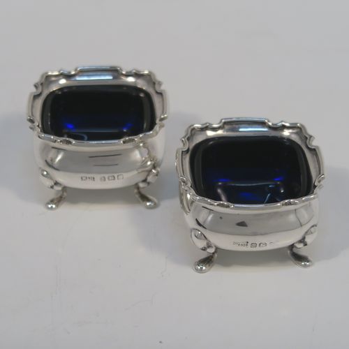 A very pretty pair of Antique Sterling Silver salt cellars, having plain square bellied bodies with with Chippendale style borders, blue glass liners, and sitting on four foliate feet, together with their original salt spoons, and all in their original light blue satin and dark-blue velvet-lined presentation box. This beautiful pair of silver salt cellars and spoons were made by Walker and Hall of Birmingham in 1923. The dimensions of these fine hand-made antique silver salt cellars are 5 cms (2 inches) square, height 8 cms (1.25 inches), and with a total weight of approx. 68g (2.2 troy ounces).