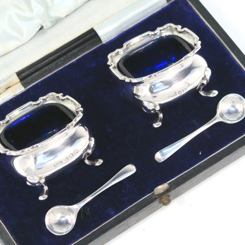 A very pretty pair of Antique Sterling Silver salt cellars, having plain square bellied bodies with with Chippendale style borders, blue glass liners, and sitting on four foliate feet, together with their original salt spoons, and all in their original light blue satin and dark-blue velvet-lined presentation box. This beautiful pair of silver salt cellars and spoons were made by Walker and Hall of Birmingham in 1923. The dimensions of these fine hand-made antique silver salt cellars are 5 cms (2 inches) square, height 8 cms (1.25 inches), and with a total weight of approx. 68g (2.2 troy ounces).