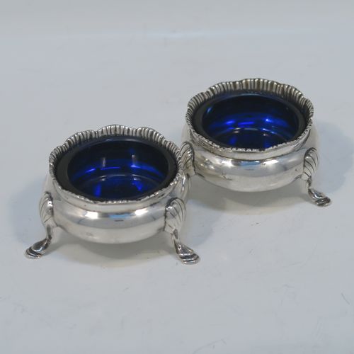A very handsome pair of Antique Sterling Silver salt cellars, having plain round bellied bodies, with blue-glass liners, applied shaped gadroon borders, and all sitting on three cast hoof feet with reeded shoulders. These elegant silver salt cellars were made by Stokes and Ireland of Chester in 1919. The dimensions of these fine hand-made antique silver salt cellars are diameter 6 cms (2.3 inches), height 3.5 cms (1.3 inches), and they weigh a total of approx. 99g (3.2 troy ounces).   
