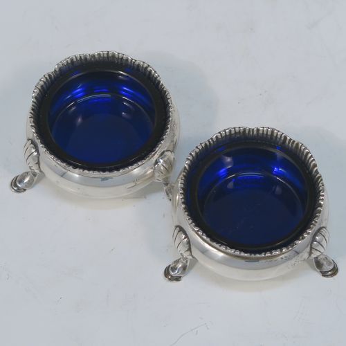 A very handsome pair of Antique Sterling Silver salt cellars, having plain round bellied bodies, with blue-glass liners, applied shaped gadroon borders, and all sitting on three cast hoof feet with reeded shoulders. These elegant silver salt cellars were made by Stokes and Ireland of Chester in 1919. The dimensions of these fine hand-made antique silver salt cellars are diameter 6 cms (2.3 inches), height 3.5 cms (1.3 inches), and they weigh a total of approx. 99g (3.2 troy ounces).