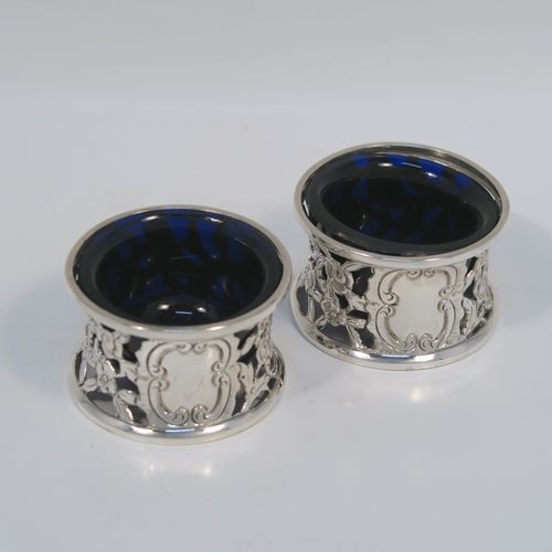 A very unusual and pretty pair of Irish Antique Victorian Sterling Silver salt cellars, in the shape of miniature potato or dish rings, having round bodies with hand-chased and hand-pierced concave shaped sides, together with hand-blown blue glass liners. These interesting antique silver salt cellars in a Potato dish ring style were made by Samuel Le Bas of Dublin in 1895. The dimensions of these fine hand-made silver salt cellars are diameter 5 cms (2 inches), height 3 cms (1.25 inches), and they weigh a total of approx. 65g (2 troy ounces).   