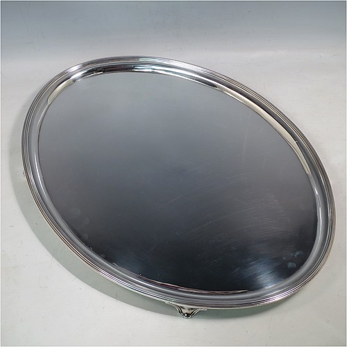 A large Antique Georgian Sterling Silver salver, having an oval body, with a plain burnished ground, an applied Reeded border, and sitting on four cast scroll feet. Made by William Bennett (Possibly) of London in 1801. The dimensions of this fine hand-made silver salver are length 46 cms (18 inches), width 35 cms (13.75 inches), and it weighs approx. 1,735g (56 troy ounces).