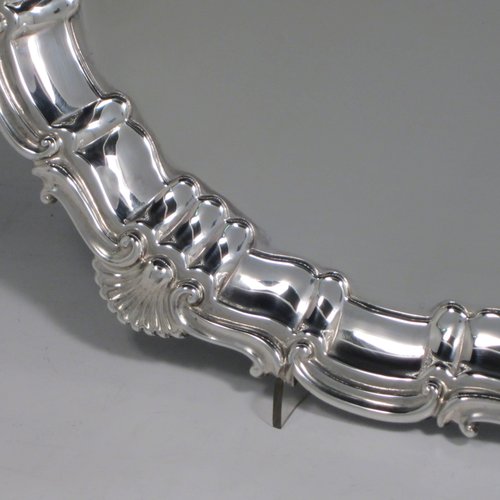 A Sterling silver salver, having a round body, with a plain burnished ground, an applied Shell & Scroll border, and sitting on three shell feet. Made by Walker and Hall of Sheffield in 1919. The dimensions of this fine hand-made silver salver are diameter 31 cms (12 inches), and it weighs approx. 658g (21 troy ounces).