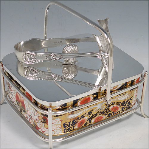 An Antique Victorian Silver Plated and fine China sardine dish, having a rectangular bone China body with hand-painted gold, blue, and orange scroll and floral decoration, all sitting in a plain wire-work galleried frame, a lift-off lid with cast conch shell finial, a plain handle, and all sitting on four wire-work feet, and with a pair of antique silver-plated sardine server tongs in the Kings pattern. The sardine dish made by James Dixon & Sons of Sheffield in ca. 1890. The dimensions of this fine hand-made antique silver-plated and bone China sardine dish are length 14 cms (5.5 inches), width 12 cms (4.75 inches), and height (excluding handles) 7 cms (2.75 inches).