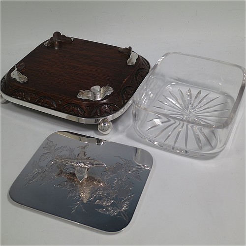 A very handsome Antique Victorian Silver Plated sardine dish, having a rectangular body with rounded corners, a cut-crystal liner sitting in a frame attached to an Oak wooden base with four ball feet, a lift-off lid with cast crossed sardines above hand-engraved floral decoration. Made in ca. 1890. The dimensions of this fine hand-made antique silver-plated sardine dish are length 18 cms (7 inches), width 15 cms (6 inches), and height 10 cms (4 inches).