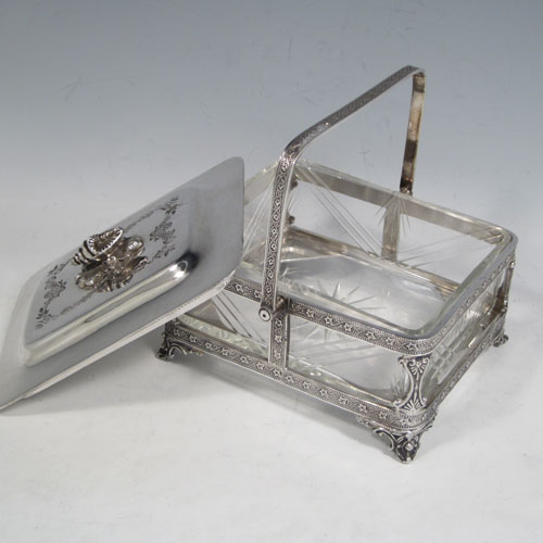 Antique Victorian silver plated sardine dish, having a rectangular body with rounded corners, a cut-crystal liner sitting in a frame which has chased ivy-work, a lift-off lid with cast conch shell finial, a floral swing handle, and all sitting on four cast foliate feet. Made by Walker and Hall of Sheffield in ca. 1880. The dimenions of this fine hand-made silver-plated sardine dish are length 14 cms (5.5 inches), width 12 cms (4.75 inches), and height (excluding handles) 8 cms (3 inches).