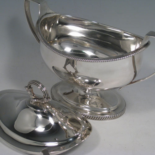 Antique Georgian George III sauce tureen, having an oval plain body, gadroon borders, lift off lid with asparagus loop handle and slot for sauce ladle, two side handles, and sitting on a pedestal foot. Made by Robert and Samuel Hennell of London in 1805. Length 21.5 cms (8.5 inches), width 11 cms (4.3 inches), height 18 cms (6.3 inches). Total weight approx. 545g (17.6 troy ounces).