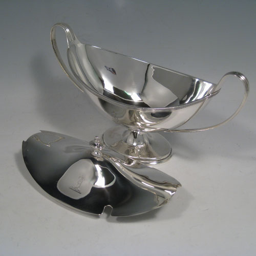 Antique Edwardian sterling silver sauce tureen, having a neoclassical boat-shaped body with reeded border, a lift-off cover with urn finial, two loop handles, all sitting on a pedestal foot. Made by Thomas Bradbury of London in 1904. Height 13 cms (5 inches), length 24 cms (9.5 inches), width 10 cms (4 inches). Total weight approx. 375g (12.1 troy ounces).