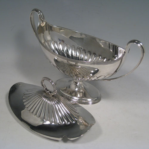 Antique Georgian sterling silver sauce tureen, having a neoclassical boat-shaped body with reeded borders and hand-chased half-fluted decoration, a lift-off cover with loop handle finial, all sitting on a pedestal foot. Made by Henry Chawner of London in 1795. Height 17 cms (6.75 inches), length 24 cms (9.5 inches), width 10 cms (4 inches). Total weight approx. 561g (18.1 troy ounces). Please note that this item is crested.