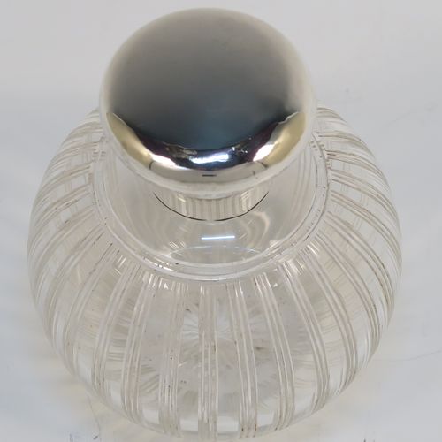 An elegant Antique Sterling Silver and hand-cut crystal large table scent bottle, having a plain round mount, a plain round hinged lid, an internal stopper, and a hand-cut crystal round main body with reeded decoration, and sitting on a flat base with a star-cut. This handsome antique silver and crystal scent bottle was made by William Comyns of Birmingham in 1913. The dimensions of this fine hand-made antique silver and crystal scent bottle are height 10 cms (4 inches), and diameter 9 cms (3.5 inches).   