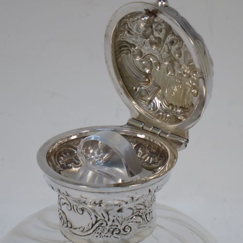 A very pretty and unusual pair of Antique Edwardian Sterling Silver and hand-cut crystal table scent bottles, having round mounts with hinged lids and internal stoppers, the lids with hand-chased figural scene decoration and push-button snap fits. The crystal bodies with rounded square cross-sections and swirl fluted decoration, and all sitting on flat bases. Made by William Comyns of London in 1907. The dimensions of these fine hand-made antique silver and crystal scent bottles are height 12.5 cms (5 inches), and 8.5cms (3.3 inches) square.  