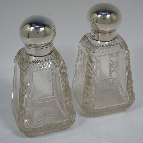 A very pretty and unusual pair of Antique Victorian Sterling Silver and hand-cut crystal table scent bottle, having plain round mounts  with hinged lids, gold-gilt interiors and internal stoppers. The crystal bodies with square cross-sections and tapering sides having clear side panels and hobnail cut edges, and all sitting on star-cut bases. Made by John Grinsell and Co., of London in 1898. The dimensions of these fine hand-made antique silver and crystal scent bottles are height 14.5 cms (5.75 inches), and 7cms (2.75 inches) square at base.    