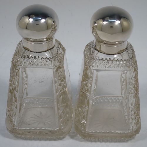 A very pretty and unusual pair of Antique Victorian Sterling Silver and hand-cut crystal table scent bottle, having plain round mounts  with hinged lids, gold-gilt interiors and internal stoppers. The crystal bodies with square cross-sections and tapering sides having clear side panels and hobnail cut edges, and all sitting on star-cut bases. Made by John Grinsell and Co., of London in 1898. The dimensions of these fine hand-made antique silver and crystal scent bottles are height 14.5 cms (5.75 inches), and 7cms (2.75 inches) square at base.    