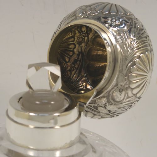 A very large and pretty pair of Antique Victorian Sterling Silver and hand-cut crystal table scent bottles, having hinged lids with gold-gilt interiors and hand-chased floral decoration, with removable internal stoppers, and hand-cut crystal main bodies. These beautiful antique silver and crystal scent bottles were made by Alfred Fuller of London in 1892. The dimensions of these fine hand-made antique silver and crystal scent bottles are height 18.5 cms (7.25 inches), width 12.5 cms (5 inches), and depth 9 cms (3.5 inches).