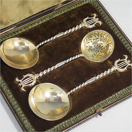 An Antique Victorian Sterling Silver and gold-gilt serving spoon set, consisting of a pair of serving spoons and a sugar sifting ladle, having cast handles with twisted stems and Lyre shaped terminals, and with gold-gilt bowls, and all sitting in an original olive green satin and velvet-lined presentation box. Made by Holland, Aldwinckle, & Slater of London in 1895. The dimensions of this fine hand-made set of antique silver serving spoons are length 17 cms (6.75 inches), and they weigh a total of approx. 154g (5 troy ounces).