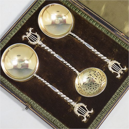An Antique Victorian Sterling Silver and gold-gilt serving spoon set, consisting of a pair of serving spoons and a sugar sifting ladle, having cast handles with twisted stems and Lyre shaped terminals, and with gold-gilt bowls, and all sitting in an original olive green satin and velvet-lined presentation box. Made by Holland, Aldwinckle, & Slater of London in 1895. The dimensions of this fine hand-made set of antique silver serving spoons are length 17 cms (6.75 inches), and they weigh a total of approx. 154g (5 troy ounces).