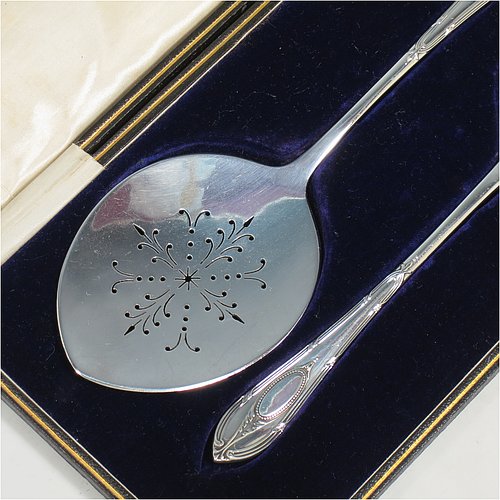 An Antique Sterling Silver serving spoon and fork, having hand-chased neoclassical pattern handles, the spoon with a hand-pierced blade, and the fork with five hand-cut tines, and all sitting in their original cream satin and dark blue velvet-lined presentation box. Made by Roberts & Belk of Sheffield in 1913. The dimensions of this fine hand-made antique pair of serving spoon and fork are length 24cms (9.5 inches), and they weigh a total of approx. 222g (7.2 troy ounces).
