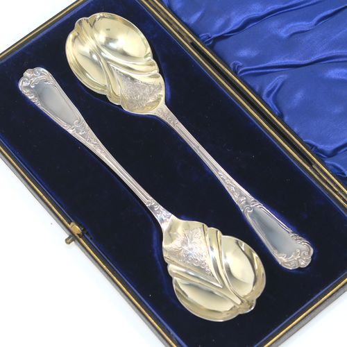 A beautiful pair of Antique Edwardian Sterling Silver serving spoons, having handles with double-struck floral and scroll-work in a Louis style pattern handles, and fluted oval bowls with a gold-gilt wash and hand-engraved floral work, all in their original dark blue satin and velvet-lined presentation box. These wonderful silver serving spoons were made by Thomas Brabury of Sheffield in 1910. The dimensions of this fine hand-made pair of antique silver serving spoons are length 19cms (7.5 inches), and they weigh a total of approx. 97g (3 troy ounces).
