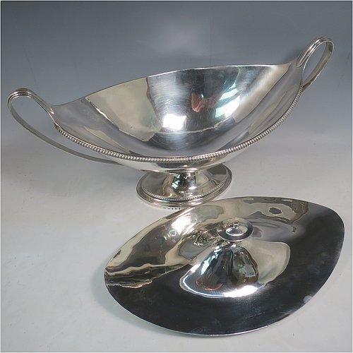 An Antique Georgian Sterling Silver large soup tureen in a boat-shape neoclassical style, having a very plain oval body with a pull-off lid and an urn-shaped finial, with applied gadroon borders, two reeded scroll side-handles, and all sitting on a pedestal foot. Made by Cornelius Bland of London in 1789. The dimensions of this fine hand-made antique silver soup tureen and cover are height 28 cms (11 inches), length including handles 52 cms (20.5 inches), width 25.5 cms (10 inches), and it weighs approx. 2,850g (92 troy ounces).