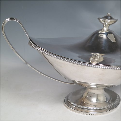 An Antique Georgian Sterling Silver large soup tureen in a boat-shape neoclassical style, having a very plain oval body with a pull-off lid and an urn-shaped finial, with applied gadroon borders, two reeded scroll side-handles, and all sitting on a pedestal foot. Made by Cornelius Bland of London in 1789. The dimensions of this fine hand-made antique silver soup tureen and cover are height 28 cms (11 inches), length including handles 52 cms (20.5 inches), width 25.5 cms (10 inches), and it weighs approx. 2,850g (92 troy ounces).