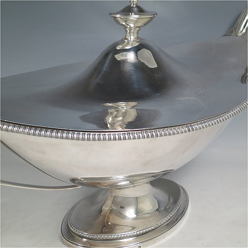 An Antique Georgian Sterling Silver large soup tureen in a boat-shape neoclassical style, having a very plain oval body with a pull-off lid and an urn-shaped finial, with applied gadroon borders, two reeded scroll side-handles, and all sitting on a pedestal foot. Made by Cornelius Bland of London in 1789. The dimensions of this fine hand-made antique silver soup tureen and cover are height 28 cms (11 inches), length including handles 52 cms (20.5 inches), width 25.5 cms (10 inches), and it weighs approx. 2,850g (92 troy ounces).