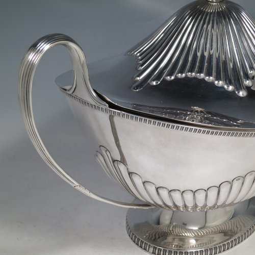 An Antique Edwardian Sterling silver soup tureen, having a pull-off lid with an urn-shaped finial and cut-out slot for a ladle, with hand-chased half-fluted decoration, applied gadroon borders, two reeded scroll side-handles, and all sitting on a pedestal foot. Made by Mappin & Webb of Sheffield in 1905. The dimensions of this fine hand-made antique silver soup tureen and cover are height 25 cms (9.75 inches), length including handles 39.5 cms (15.5 inches), width 21.5 cms (8.5 inches), and it weighs approx. 1,779 (57 troy ounces).
