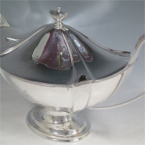 An Antique Edwardian Sterling silver Neoclassical style soup tureen, having a pull-off lid with an urn-shaped finial and cut-out slot for a ladle, with hand-chased shoulders, applied reeded borders, two reeded scroll side-handles, and all sitting on a pedestal foot. Made by Goldsmiths & Silversmiths of London in 1902. The dimensions of this fine hand-made antique silver soup tureen and cover are height 23 cms (9 inches), length including handles 38 cms (15 inches), width 20 cms (8 inches), and it weighs approx. 1,615 (52 troy ounces). Please note that this item is crested on lid and body.