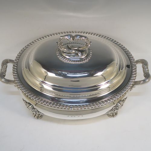 A very handsome Antique Georgian Sterling Silver Scottish soup tureen in a Regency style, having an oval plain baluster body with applied gadroon border, a domed pull-off cover with a cast anthemion leaf handle, with two cast scroll side handles, and sitting on four cast lions-paw feet with floral shoulders. This elegant antique silver soup tureen and cover was made in Edinburgh in 1815. The dimensions of this fine hand-made antique silver soup tureen are height 24 cms (9.5 inches), and width (across handles) 42 cms (16.5 inches), and it weighs approx. 3,285g (106 troy ounces). Please note that this antique Regency silver soup tureen is crested on the main body and cover.