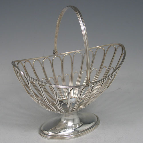 Antique Georgian sterling silver sugar basket, having an oval wire-work body, with hinged reeded swing-handle, a blue-glass liner, and sitting on a pedestal foot. Made by Robert Hennell I of London in 1792. The dimensions of this fine hand-made silver sugar basket are height (inc. handle) 18 cms (7 inches), length 15.5 cms (6 inches), and it weighs approx. 222g (7.2 troy ounces).
