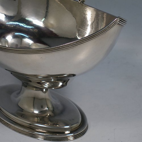 An Antique Georgian Sterling Silver sugar basket, having a plain oval bellied body, with applied reeded borders, a hinged and reeded swing-handle, and sitting on a pedestal foot. Made by Peter & Anne Bateman of London in 1798. The dimensions of this fine hand-made antique silver sugar basket are height (inc. handle) 18 cms (7 inches), length 16.6 cms (6.5 inches), and it weighs approx. 215g (7 troy ounces).